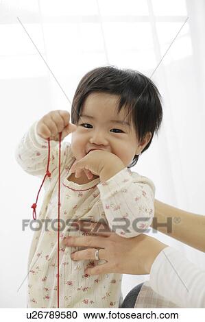Stock Image - Baby holding string and covering mouth with hand. Fotosearch