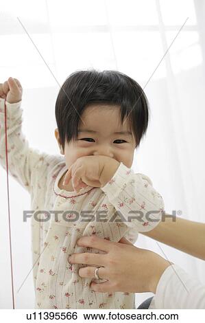 Stock Photograph - Baby holding string and covering mouth with hand. Fotosearch