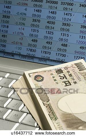 Stock Image - Bundle of Japanese currencies on laptop, close up. Fotosearch