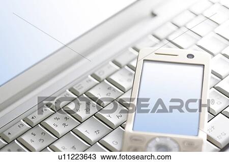 Stock Image - Cell phone on laptop keyboard. Fotosearch