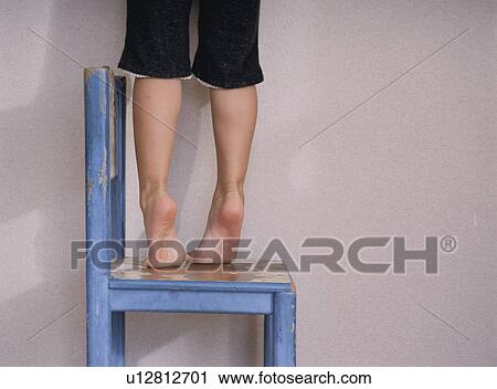 Stock Image - Child standing and reaching out on chair. Fotosearch