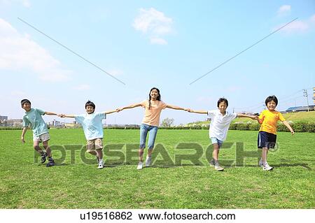 Stock Image - Children in row holding hands on field. Futako-tamagawa, Setagaya-ku, Tokyo Prefecture, Japan. Fotosearch