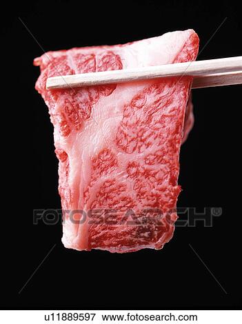 Stock Photo - Chopsticks holding slice of fresh meat, black background. Fotosearch
