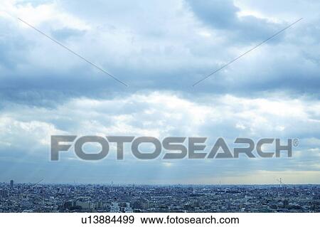 Stock Photo - Clouds and sunbeams over office buildings, Tokyo prefecture, Japan. Fotosearch