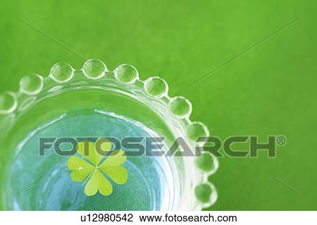 Stock Image - Four leafed clover floating on glass of water, close up, green background. Fotosearch