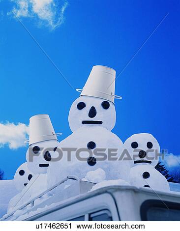Stock Image - Four snowmen on the roof of a car. Fotosearch
