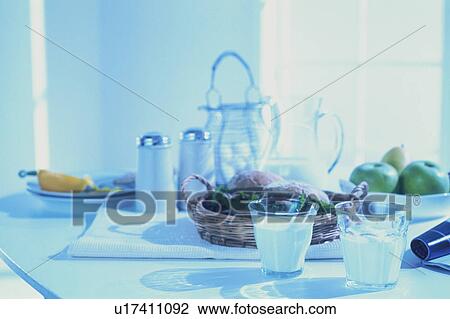 Stock Image - Glasses of milk, fresh fruit and some bread rolls for breakfast. Fotosearch