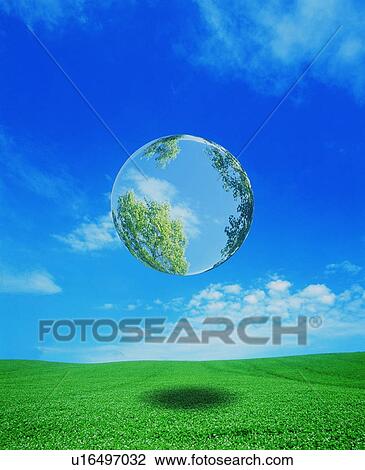 Stock Image - Globe reflecting trees floating over green field. Fotosearch