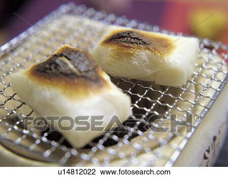 Stock Image - Grilled mochi over charcoal fire. Fotosearch