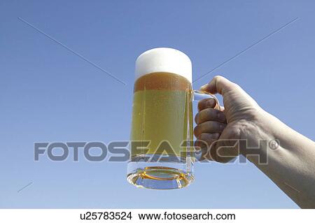 Hand holding glass of beer against blue sky, blue background View Large Photo Image Picture - Hand holding glass of beer against blue sky, blue background. Fotosearch