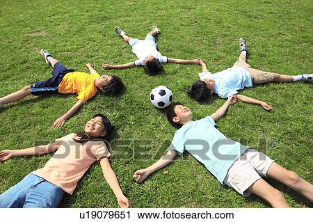 Stock Image - Happy children lying on field with soccer ball. Futako-tamagawa, Setagaya-ku, Tokyo Prefecture, Japan. Fotosearch