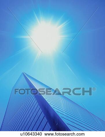 Stock Image - Low angle view of skyscraper and large sun. Fotosearch