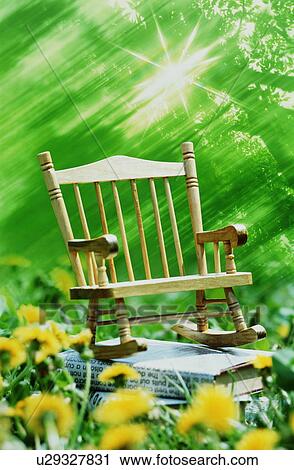 Stock Image - Miniature rocking chair on books outside amongst flowers and trees. Fotosearch