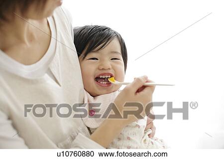 Stock Image - Mother spoon feeding baby girl. Fotosearch