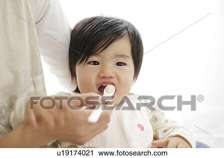 Stock Image - Mother spoon feeding baby girl. Fotosearch