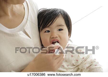 Stock Photograph - Mother spoon feeding baby girl. Fotosearch