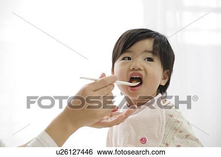 Stock Photograph - Mother spoon feeding baby girl. Fotosearch