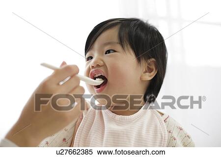 Stock Photography - Mother spoon feeding baby girl. Fotosearch