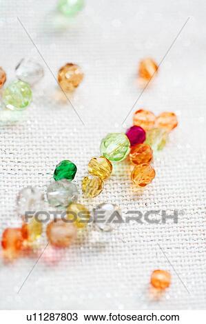 Stock Image - Multicoloured beads on shiny white fabric. Fotosearch