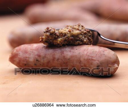 Picture - Mustard being spread onto a Vienna sausage. Fotosearch