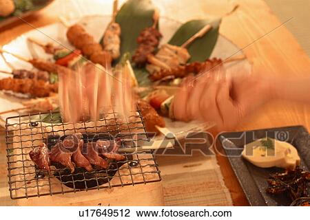 Stock Image - Person cooking skewers of meat. Fotosearch