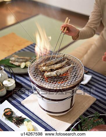 Stock Photo - Person cooking smelt on charcoal brazier. Fotosearch