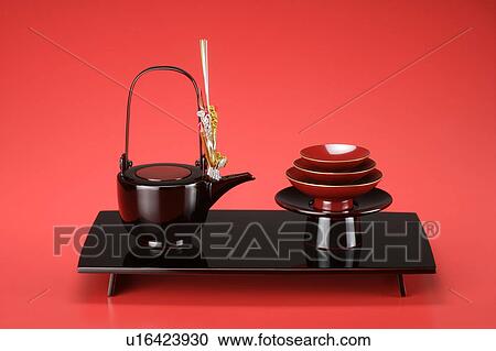 Stock Image - Pile of Sake cups and teapot, red background. Fotosearch