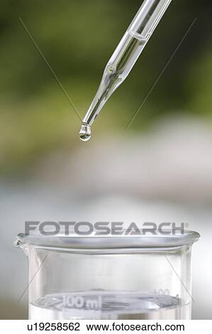 Stock Image - Pipette dropping liquid into beaker. Fotosearch