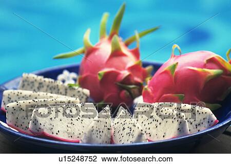Stock Image - Plate of sliced pitaya, blue background. Fotosearch