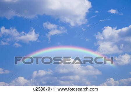 Stock Image - Rainbow in blue sky with clouds. Fotosearch