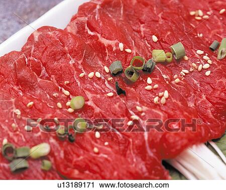 Stock Image - Raw steaks garnished with spring onion and sesame seeds. Fotosearch