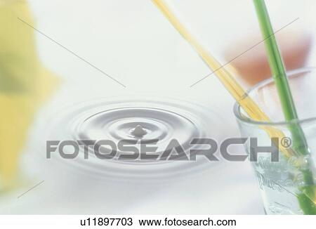 Stock Image - Rippling water and a glass with straws. Fotosearch
