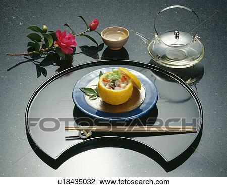 Stock Image - Sake and plate of cooked yuzu fruit, black background. Fotosearch