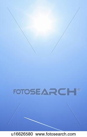 Stock Image - Sun and vapor trail in the sky, blue background. Fotosearch