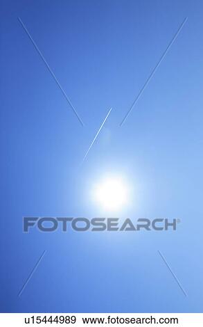 Stock Photo - Sun and vapor trail in the sky, blue background. Fotosearch