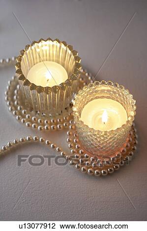 Stock Image - Tealight candles in glass holders with pearl necklace. Fotosearch
