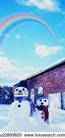 Stock Image - Two snowmen under a rainbow outside a cottage. Fotosearch