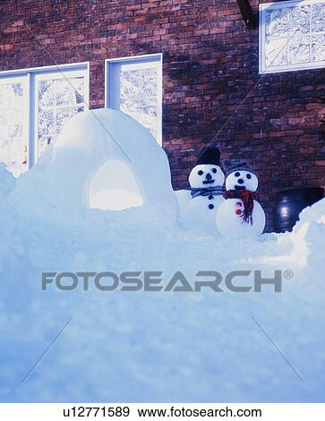 Stock Photo - Two snowmen with a snow cave behind a cottage . Fotosearch
