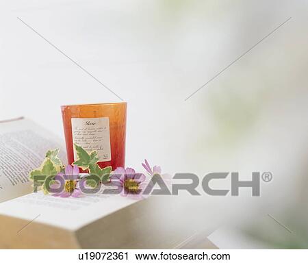 Stock Image - Wildflowers and a scented candle sitting on an open book. Fotosearch