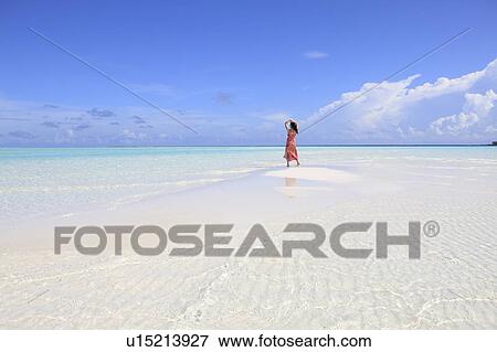 Stock Photo - Woman in shallow water at beach, looking at view, Maldive Islands. Fotosearch