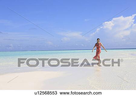 Stock Image - Woman walking through shallow water at the beach, Maldive Islands. Fotosearch