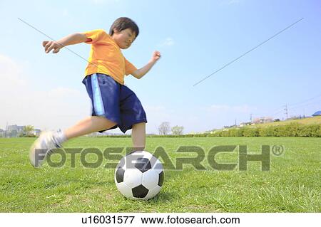 Stock Photo - Young boy kicking soccer ball on field. Futako-tamagawa, Setagaya-ku, Tokyo Prefecture, Japan. Fotosearch