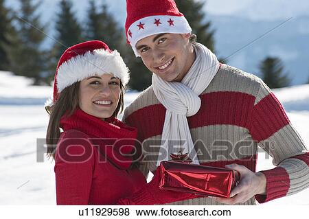 Stock Photo - Couple in Christmas outfit, giving a present. Fotosearch