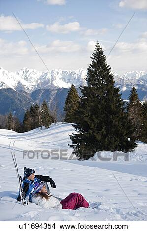 Picture - Couple sitting in snow with skis. Fotosearch