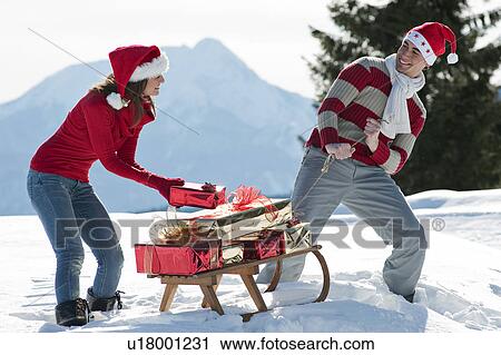 Stock Image - Couple with sleigh and presents in winter scene. Fotosearch