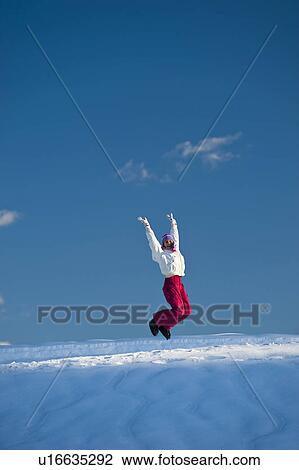 Stock Image - Young woman jumping in snow, arms outstretched. Fotosearch
