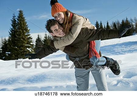 Stock Photo - Young woman riding piggyback on young man in winter scene. Fotosearch