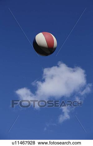 Stock Photo - Basketball in air against blue sky with cloud. Fotosearch
