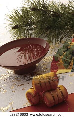 Stock Image - Brown saki cup with pine branches, a fan and rice bags. Fotosearch