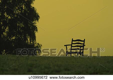 Stock Image - Chair in field against yellow sky. Fotosearch
